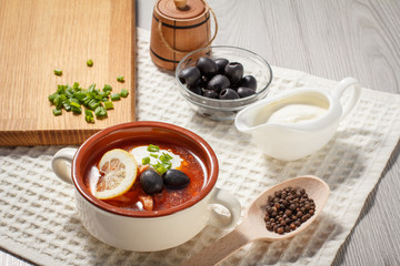 Soup saltwort with meat, potatoes, tomatoes, lemon, black olives and sour cream in ceramic soup bowl