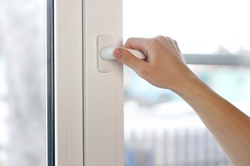 A man's hand opens a white plastic window. Close up