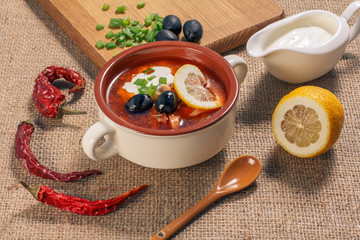 Soup saltwort with meat, potatoes, tomatoes, lemon, black olives and sour cream in ceramic soup bowl
