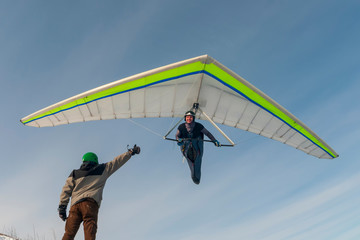 Smiling hang glider pilot fly with his wing low above ground.