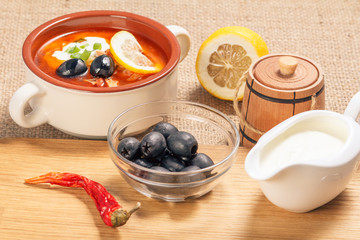 Bowl with olives, dried red pepper on cutting board and ceramic soup bowl with saltwort, sauceboat and cut lemon.