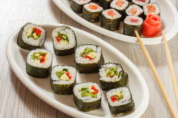 Different sushi rolls on ceramic plates and chopsticks with pickled ginger.