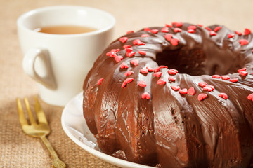 Homemade chocolate cake decorated with small caramel hearts and cup of tea.