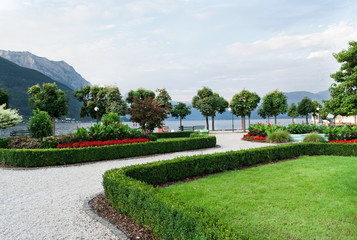 Obraz premium View of the mountains, the lake and the embankment of the city with trimmed trees, shrubs, lawn and flower beds.