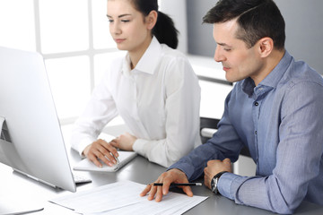 Cheerful smiling businessman and woman working with computer in modern office. Headshot at meeting or workplace. Teamwork, partnership and business concept 
