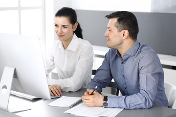 Obraz premium Cheerful smiling businessman and woman working with computer in modern office. Headshot at meeting or workplace. Teamwork, partnership and business concept 