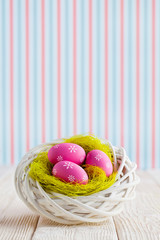 Easter eggs in the nest and wooden table on patterned background