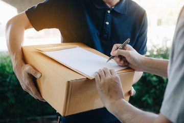 Delivery young man standing at the door of home and carrying parcels for young male to signing.