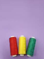Colored sewing thread on purple frosted fabric background. Selective focus.