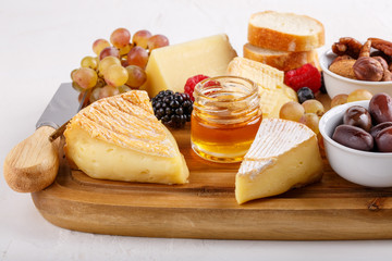 Cheese plate. French cheese with nuts, grape, berries, dried fruits and honey on cutting board on white. Camembert, Livarote, Pont-L'eveque cheese from Normandy and comte cheese.