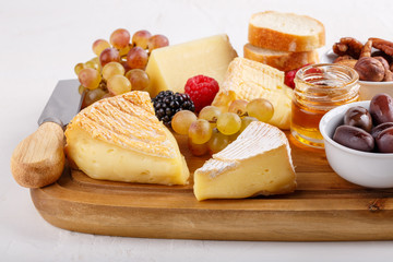 Cheese plate. French cheese with nuts, grape, berries, dried fruits and honey on cutting board on white. Camembert, Livarote, Pont-L'eveque cheese from Normandy and comte cheese.