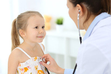 Doctor examining a little girl by stethoscope. Happy smiling child patient at usual medical inspection. Medicine and healthcare concepts