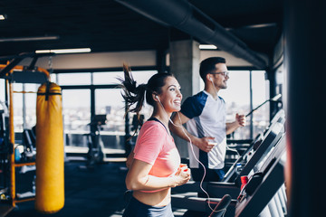 Young fit man and woman running on treadmill in modern fitness gym. - Powered by Adobe