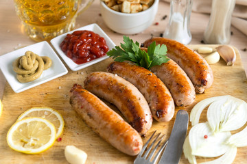 fried meat sausages on cutting Board, ketchup, mustard, onion, greens, lemon, garlic, light beer mug