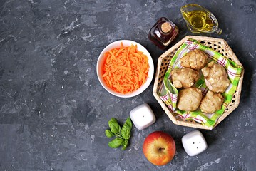 Ingredients for cooking vegetable salad: raw Jerusalem artichoke in wicker basket, raw grated carrots, apple, olive oil, red wine vinegar, fresh basil, salt, pepper. Top view. Copy space.