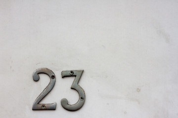 House number 23 with the twenty-three in silver on a white but dirty door and aligned with the...