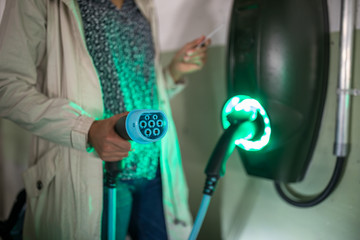 Young woman charging an electric vehicle in an underground garage equiped with e-car charger. Car...