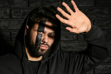 Fototapeta premium Portrait of handsome man with paint on his face against dark brick background