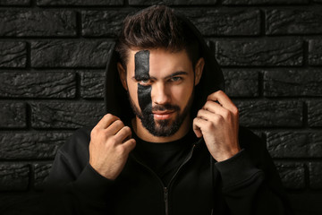 Portrait of handsome man with paint on his face against dark brick background