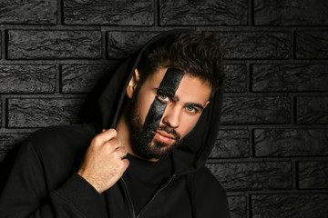 Portrait of handsome man with paint on his face against dark brick background