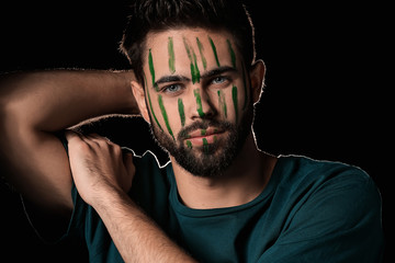 Portrait of handsome man with paint on his face against dark background