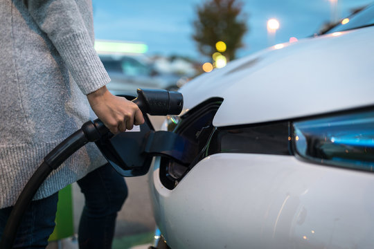 Young Woman Charging An Electric Vehicle. Car Sharing Concept.