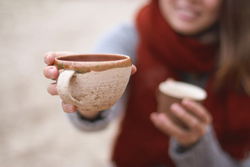 smiling girl holds two cups, one of which she hold out into the frame