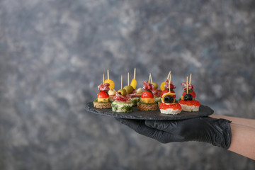 Chef holding slate plate with tasty canapes on grey background