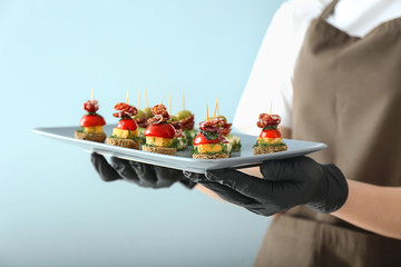 Chef holding plate with tasty canapes on light background