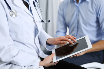 Female doctor using touchpad or tablet computer while consulting man patient in hospital. Medicine and healthcare concept