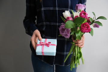 Woman with gift box and bouquet of beautiful flowers on light background