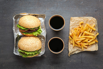 Tasty fresh burgers, cups of soda and french fries on table