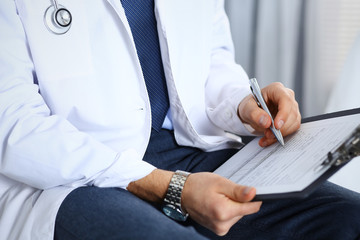 Doctor man filling up medical form on clipboard at hospital, close-up. Healthcare, insurance and medicine concept 