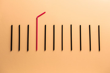 Red cocktail straw among black ones on color background. Concept of uniqueness