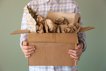 Woman holding box with paper garbage on color background
