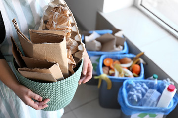 Woman holding trash bin with paper garbage indoors