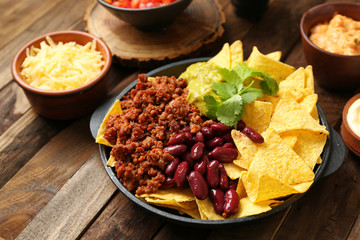 Frying pan with tasty nachos, minced meat, beans and guacamole on wooden table