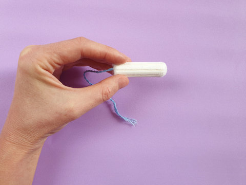 One hygienic tampon in hand. Purple background. Menstrual cycle period concept. Woman days hygiene protection.