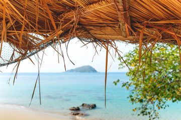 Tropical sand beach sea shore view through the straw umbrella roof. Travel vacation summer.