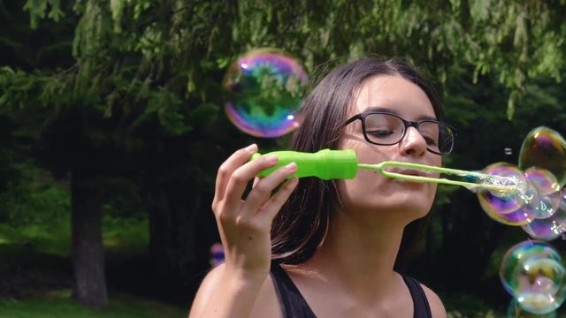 Teenage girl blowing soap bubbles and having fun in summer time. 4k hand held movement