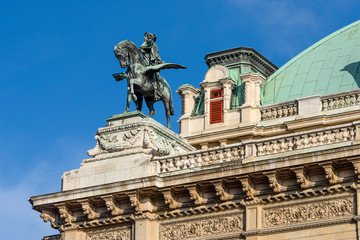 Obraz premium Austria, Vienna, Opernring: Roof top of the famous Vienna State Opera (Wiener Staatsoper) with rider on pegasus statue in the city center of the Austrian capital with blue sky - concept travel music