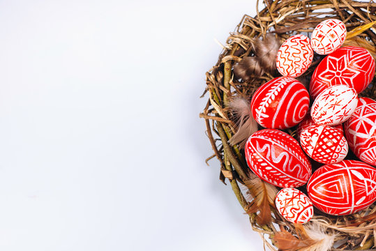Closeup Easter red eggs with folk white pattern inside bird nest on white. Top view.