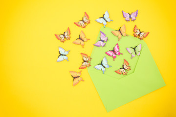 Top view of decorative, multicolored butterflies comming out of an open, green envelope from recycled paper on a vibrant yellow background. Hello Summer concept. Space for text.