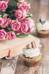 Fototapeta na wymiar Handmade chocolate muffins with decorations. Book and a bouquet of roses, blurred background