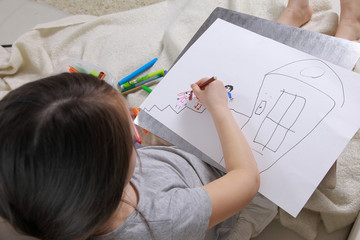 Girl in bright clothing draws a picture of the family. Light room