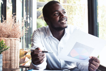 African business man holding pen and paperwork and thinking in Cafe.