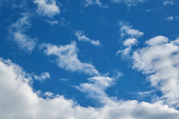 White Cumulus and Cirrus clouds in a clear blue sky. There's a big cloud below. On top of small clouds with the gaps. The wind blows light clouds.
