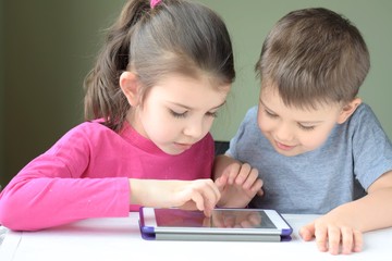 White caucasian toddler boy and beautiful girl smiling and playing together on tablet games. Portrait of a happiness little brother and sister. Happy Children play a computer game on the tablet.