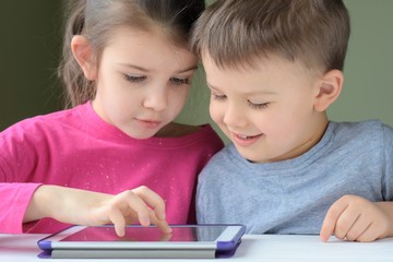White caucasian toddler boy and beautiful girl smiling and playing together on tablet games. Portrait of a happiness little brother and sister. Happy Children play a computer game on the tablet.