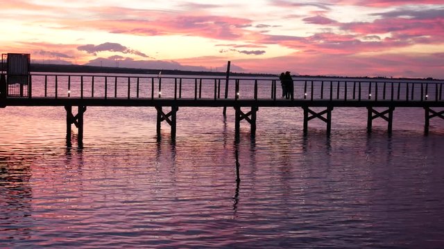 Lesina, Gargano National Park, Apulia, Italy - March 11 2019: people walk on jatty on (lake) lagoon at sunset. the red color of the twilight on the lagoon creates a beautiful effect